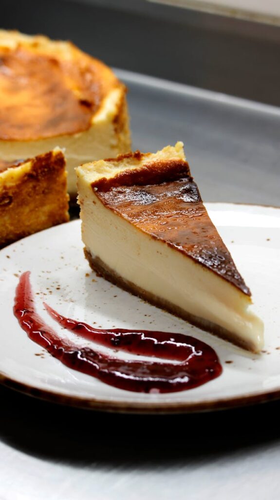 A rich Basque cheesecake slice on a plate with berry sauce, perfect for dessert lovers.